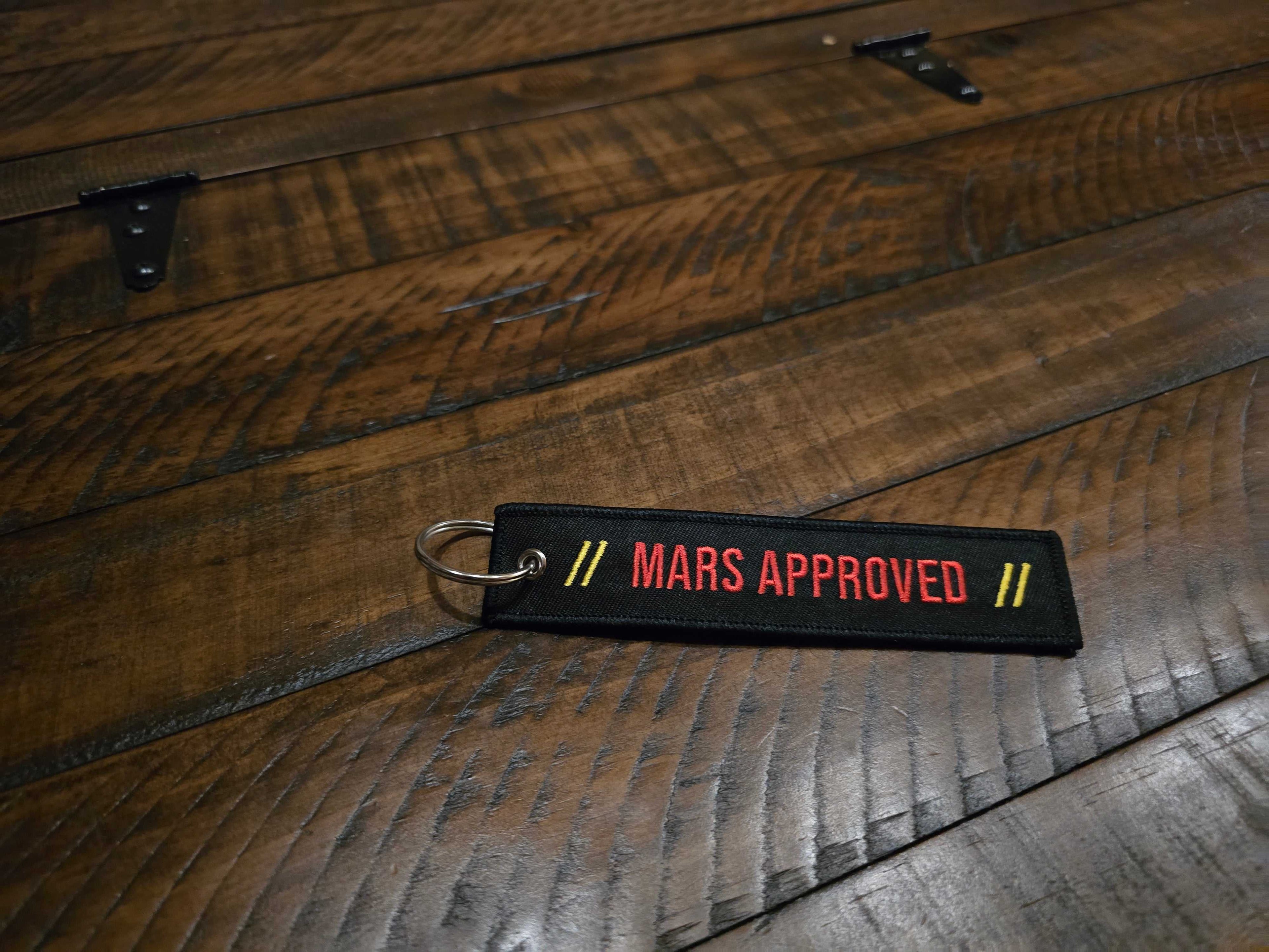 Mars Approved Flight Tag black embroidered keyring with red lettering on wooden surface