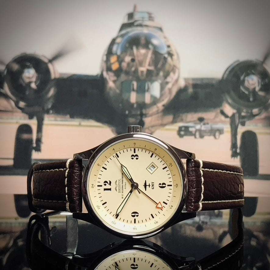 B-17 Flying Fortress tribute watch with beige dial, polished stainless steel case, and brown leather strap against B-17 bomber background