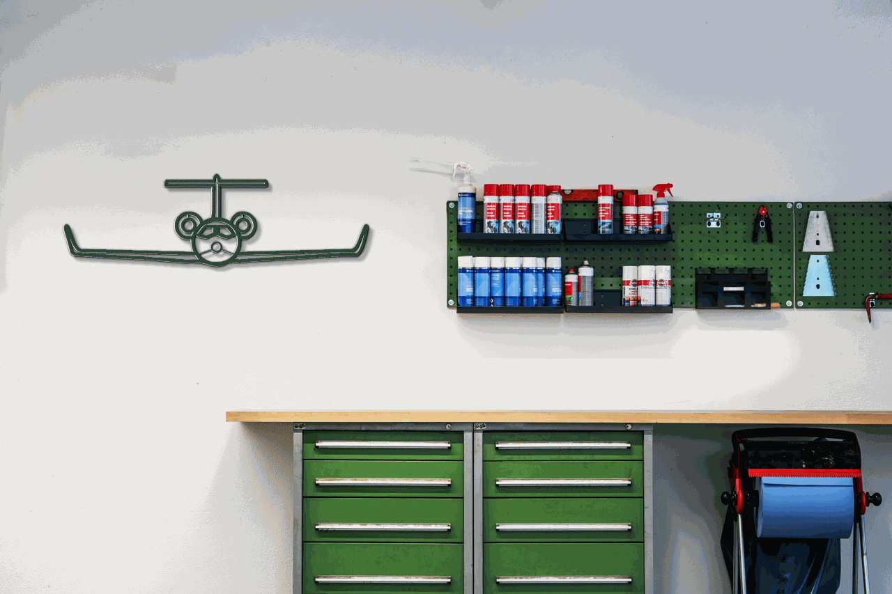 metal wall art steel silhouette airplane mounted on white wall above green workbench with organized spray paint cans and tools