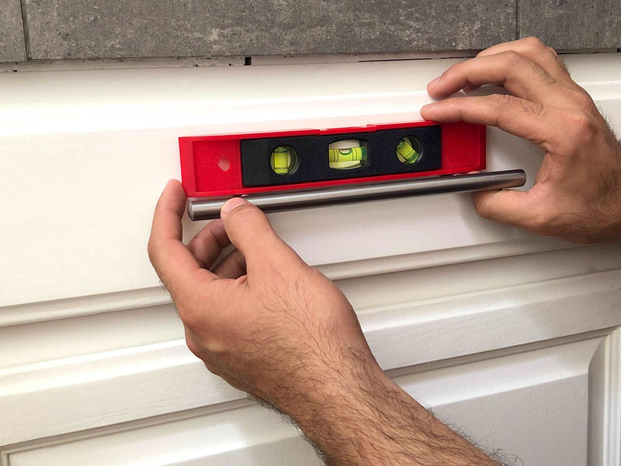 Person using red level tool on a household door handle for alignment in household tool kit use