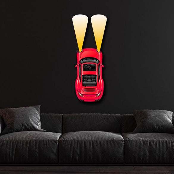 Red metal car wall art with illuminated headlights mounted on black wall above dark sofa