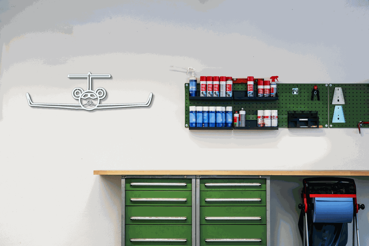metal wall art airplane silhouette made of steel displayed on white wall above green cabinets and tools in workshop