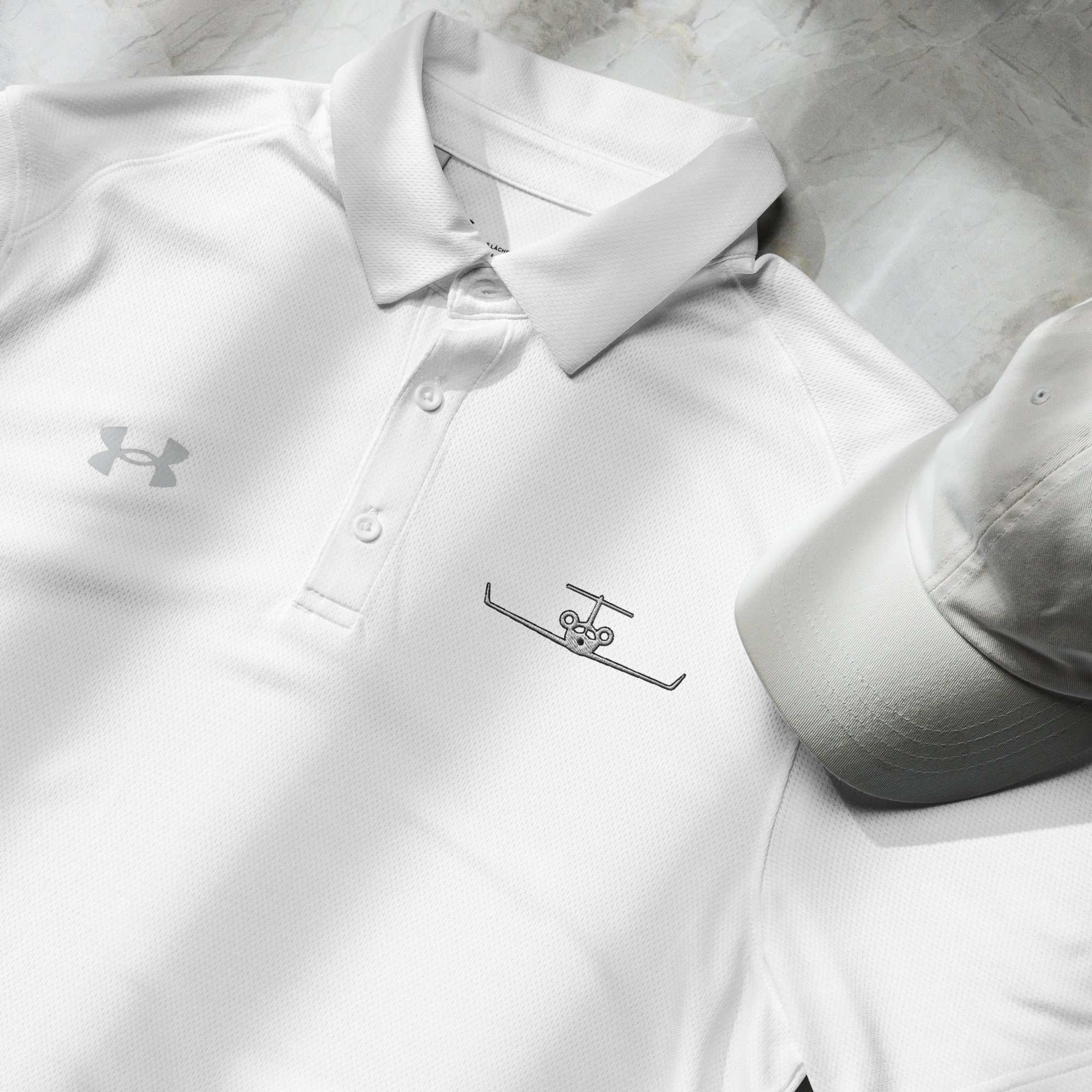 White pilot polo shirt with embroidered private jet logo and Under Armour logo next to a white cap