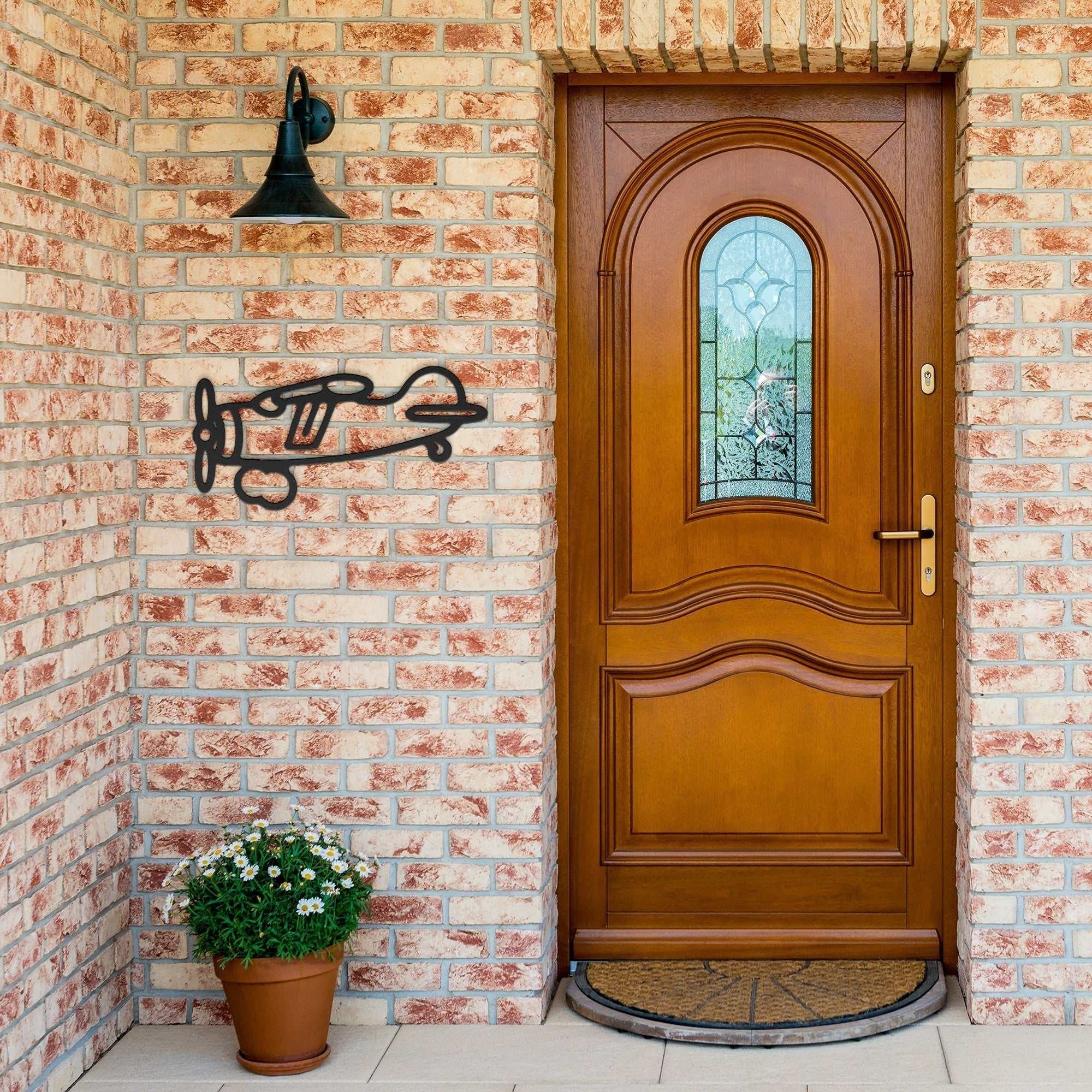 Vintage airplane metal wall art displayed on a brick wall next to a wooden door and potted flower.