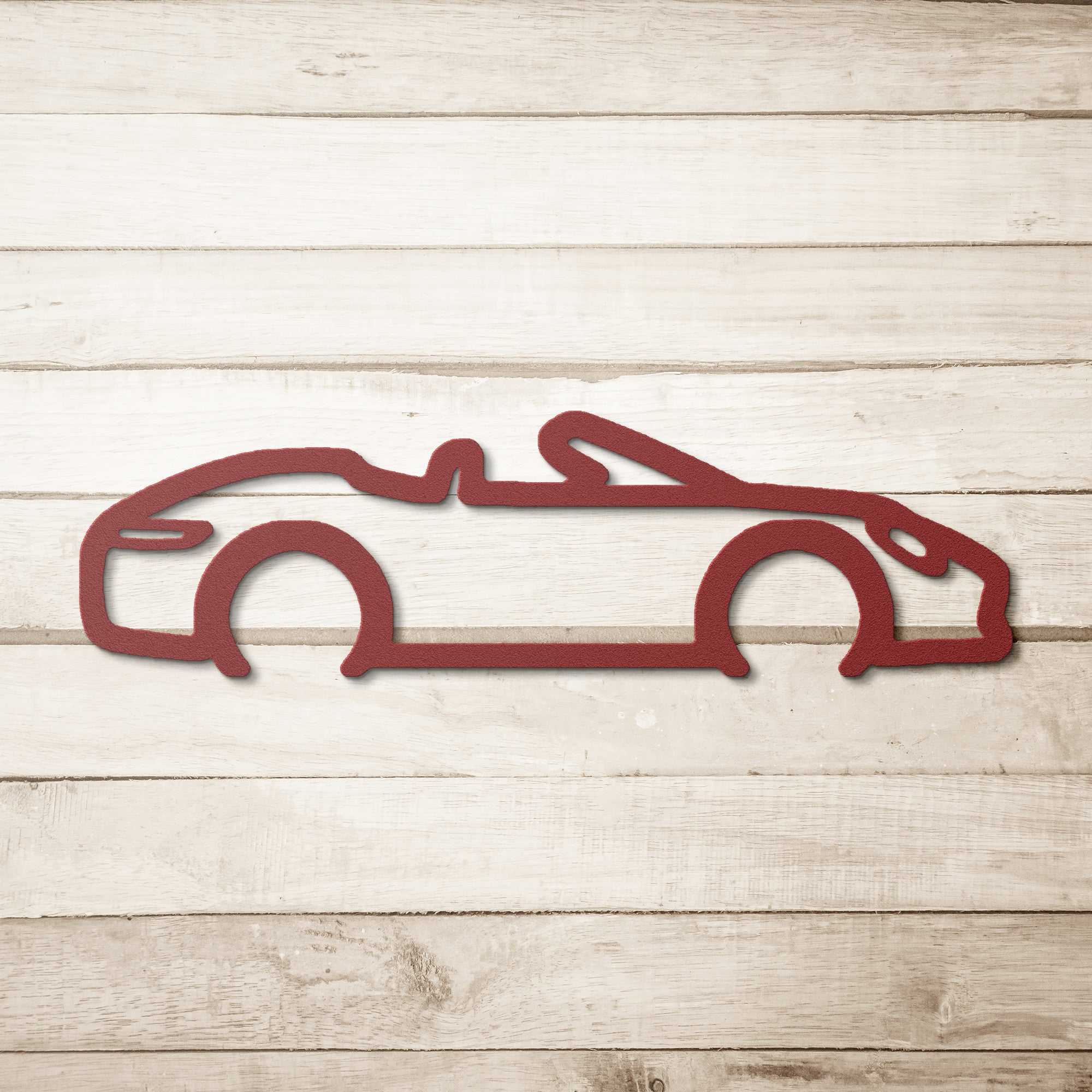 Red powder-coated steel automotive metal wall art featuring a convertible silhouette on a wooden background