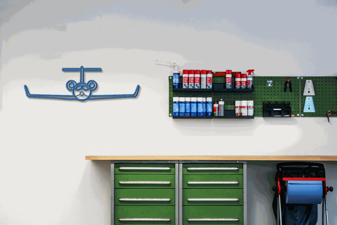 Blue metal wall art aviation silhouette above green tool cabinets in workshop