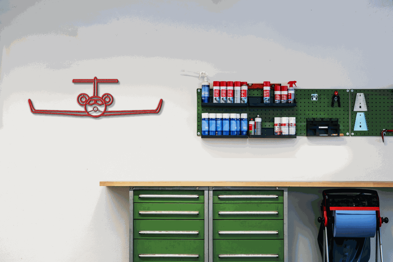 Red steel silhouette airplane metal wall art in workshop setting with tools and green cabinets