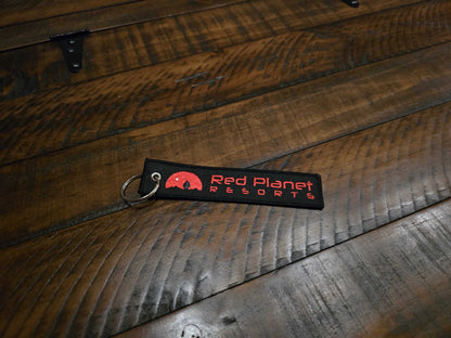 Mars Approved Flight Tag embroidered with Red Planet Resorts logo and metal keyring on wooden surface