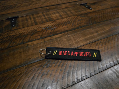 Mars Approved Flight Tag black embroidered keyring with red lettering on wooden surface