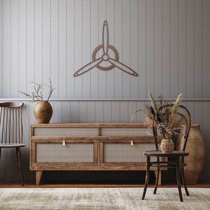 Elegant metal sign shaped like a 3-blade propeller in rustic copper finish mounted on a gray wall above a wooden sideboard in a cozy living room setting