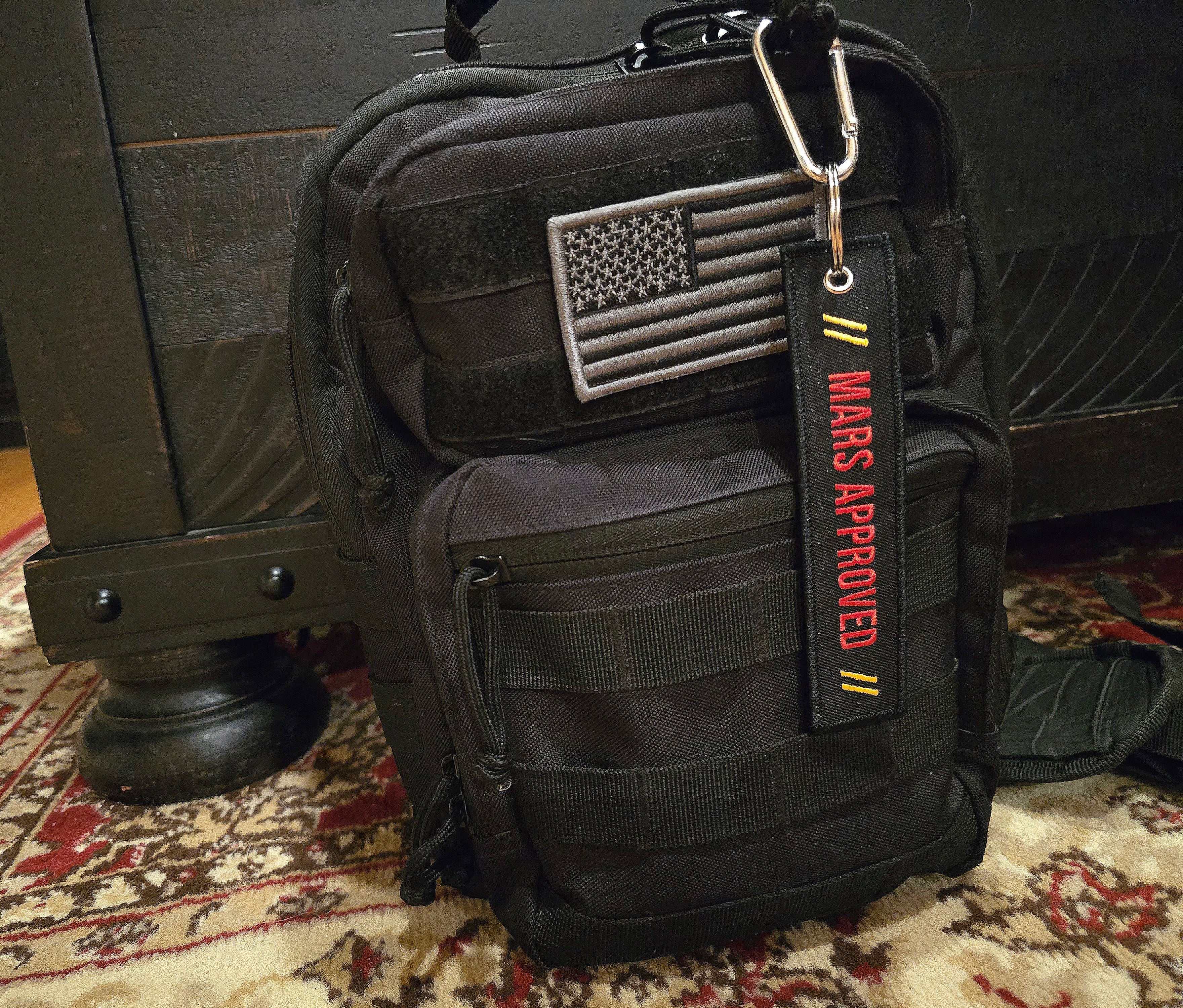 Mars Approved Flight Tag with red embroidery on black attached to black tactical backpack with American flag patch