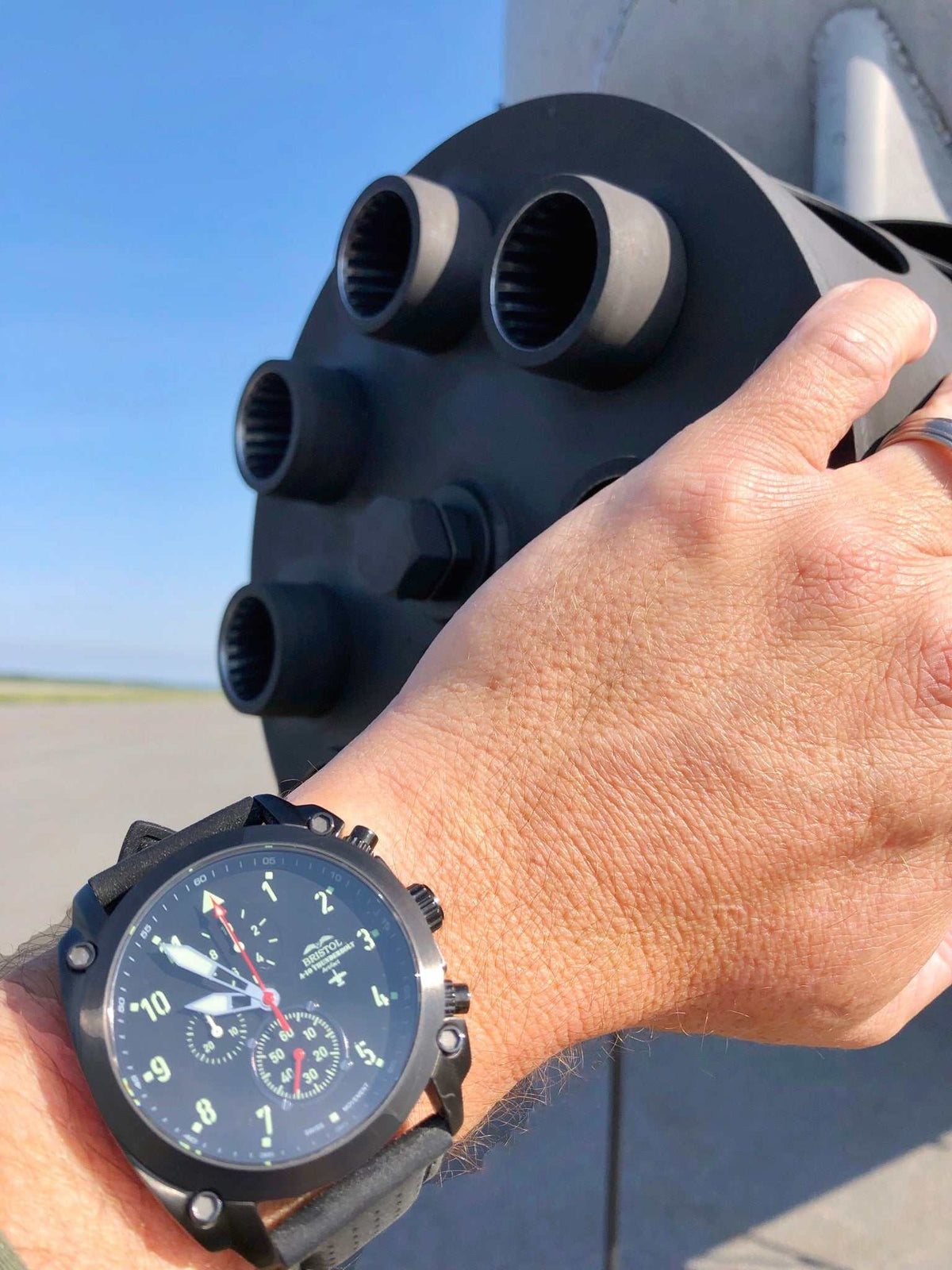 A-10 Thunderbolt tribute watch with gunmetal finish and black leather band on wrist near aircraft exhaust