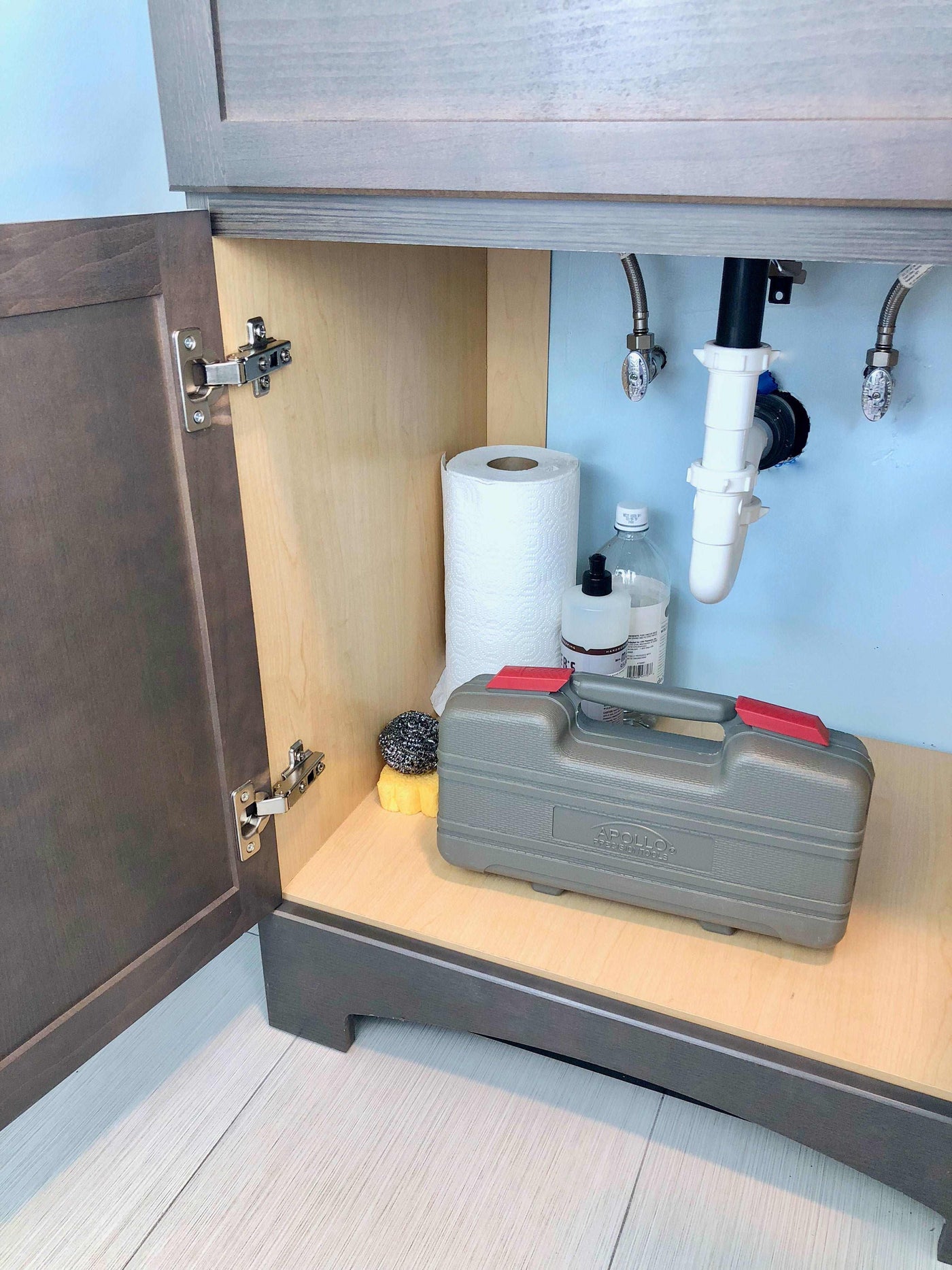 Compact gray general tool set case stored inside a dark wood under-sink cabinet for household repairs