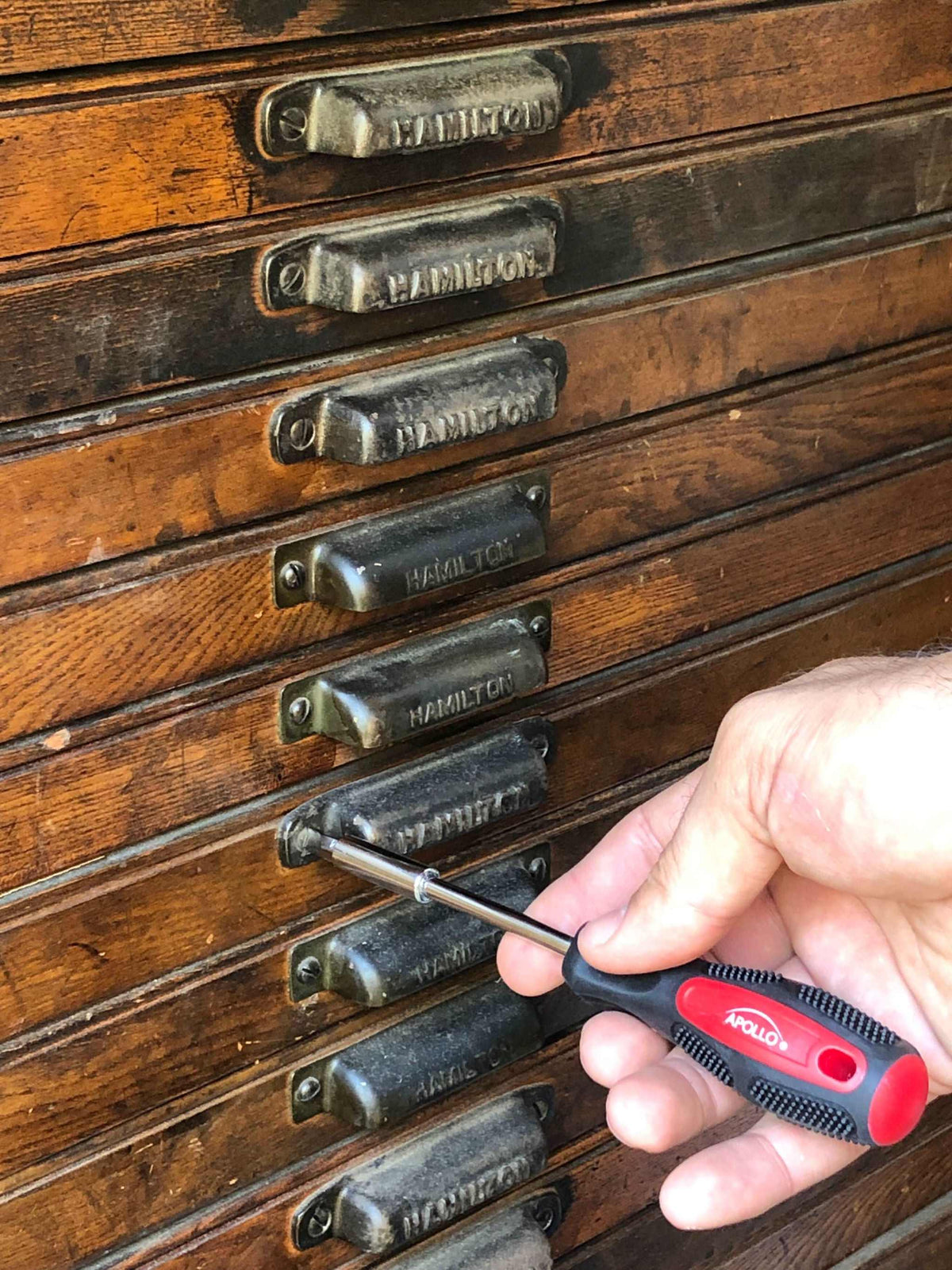 Hand using Apollo screwdriver from 71 piece household tool kit on wooden drawer handles