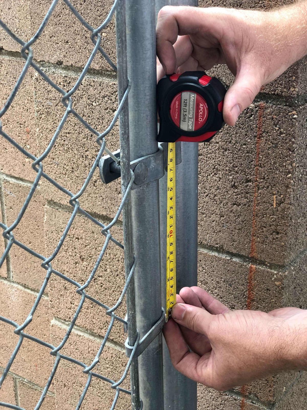 Person using a tape measure from a household tool kit to measure a metal fence post