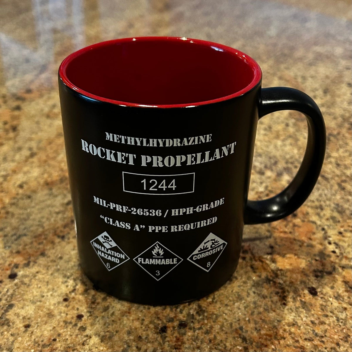 Rocket Propellant Coffee Mug styled like a NASA hydrazine fuel drum with hazard markings and red interior.