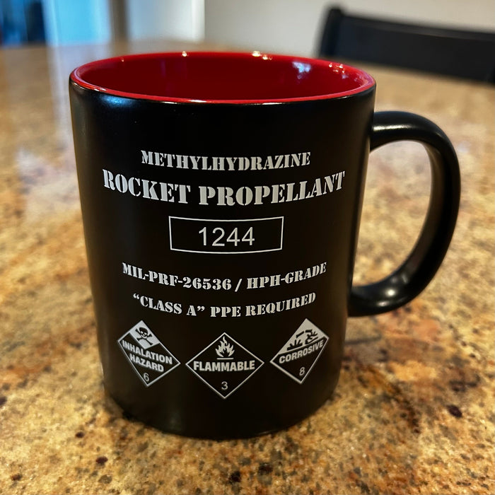 Rocket Propellant Coffee Mug shaped like a NASA hydrazine fuel drum with hazard markings and red interior.