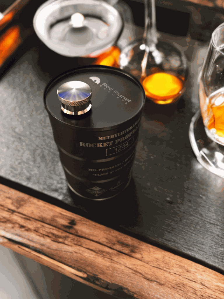 Hydrazine Barrel Flask shaped like a rocket propellant drum with NASA markings and leak-proof cap on a table with drinks