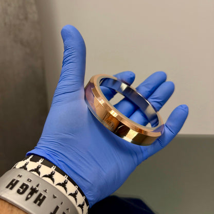 Hand wearing a blue glove holding a metallic bracelet against a neutral background