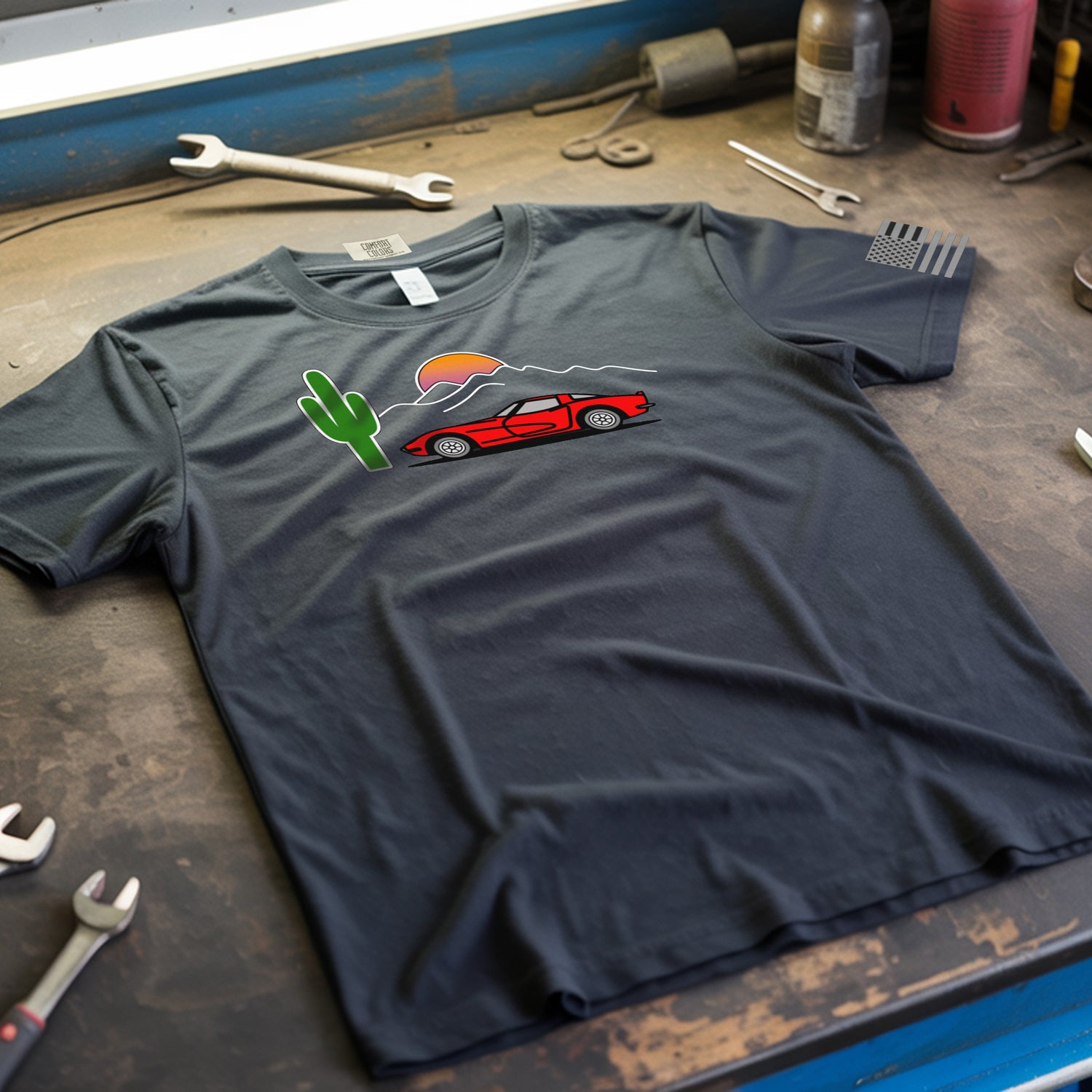 Gray t-shirt with a red car and cactus graphic on a workshop table with tools.