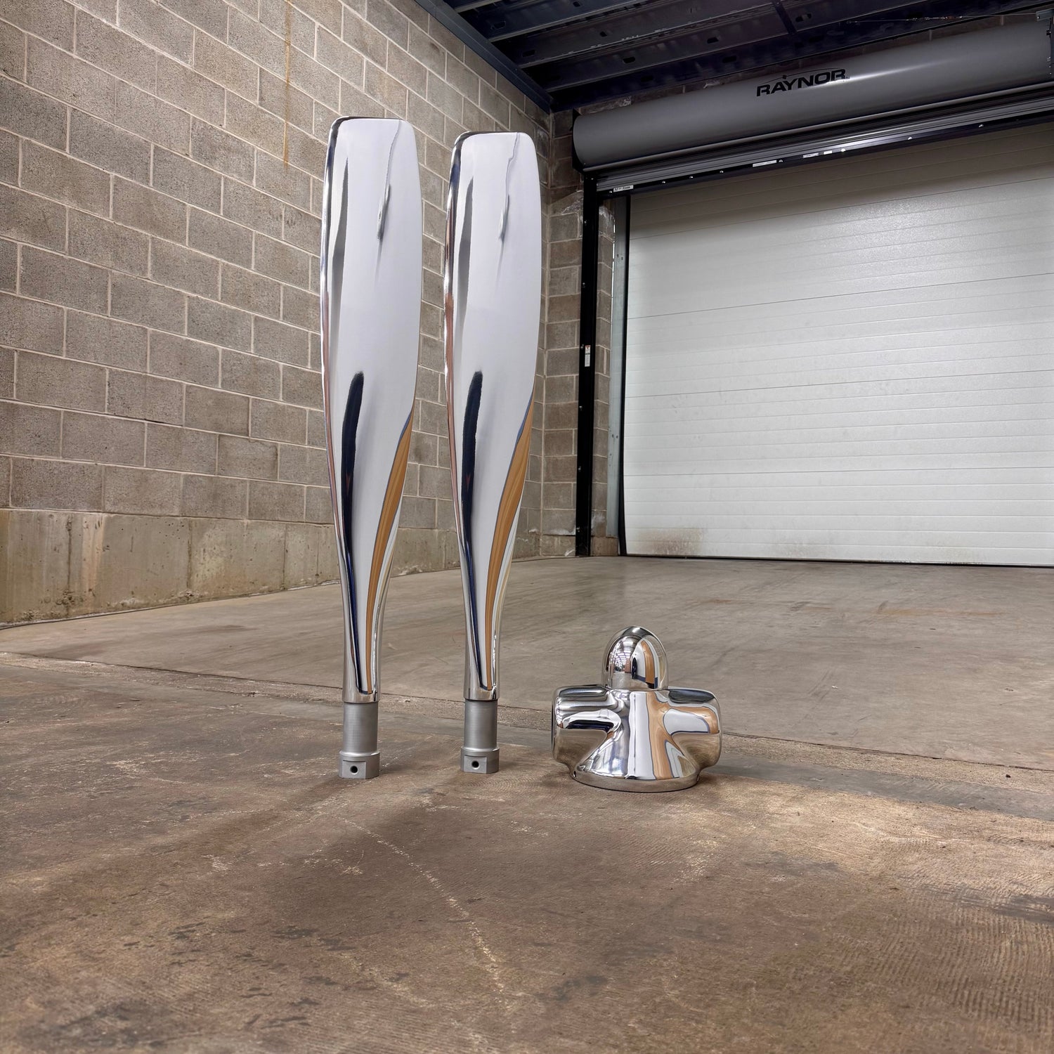 Two large metallic objects and a smaller one on a concrete floor against a brick wall.