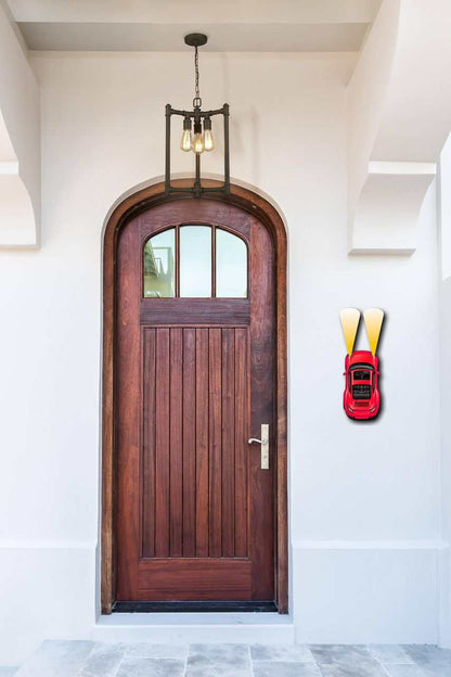 metal car wall art with red finish and bold headlights mounted beside wooden front door in modern entryway