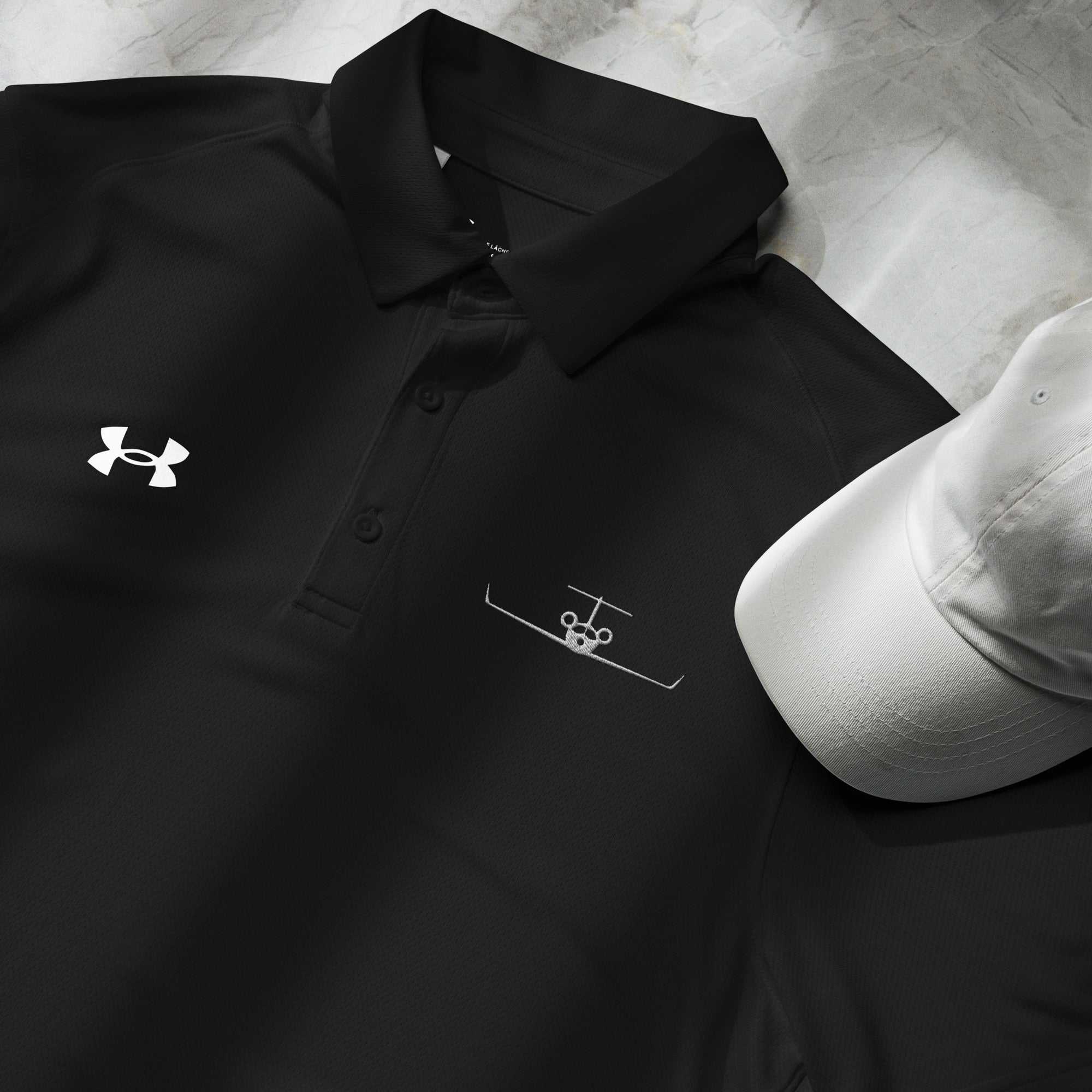 Black pilot polo shirt with embroidered private jet logo and Under Armour logo next to a white cap