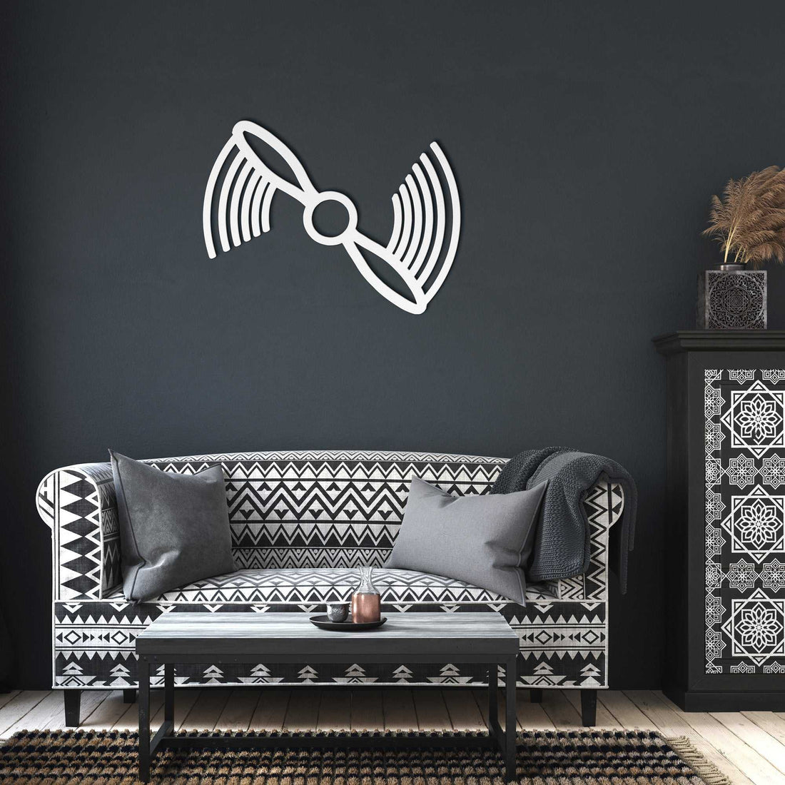White propeller metal wall art mounted on dark gray wall above black and white patterned sofa in modern living room