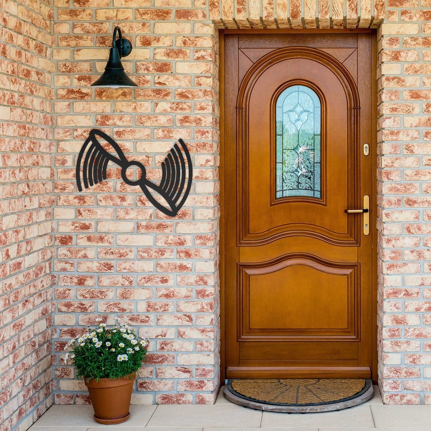 Black propeller metal wall art mounted on brick wall next to wooden front door