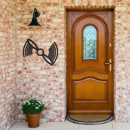 Black propeller metal wall art mounted on brick wall next to wooden front door