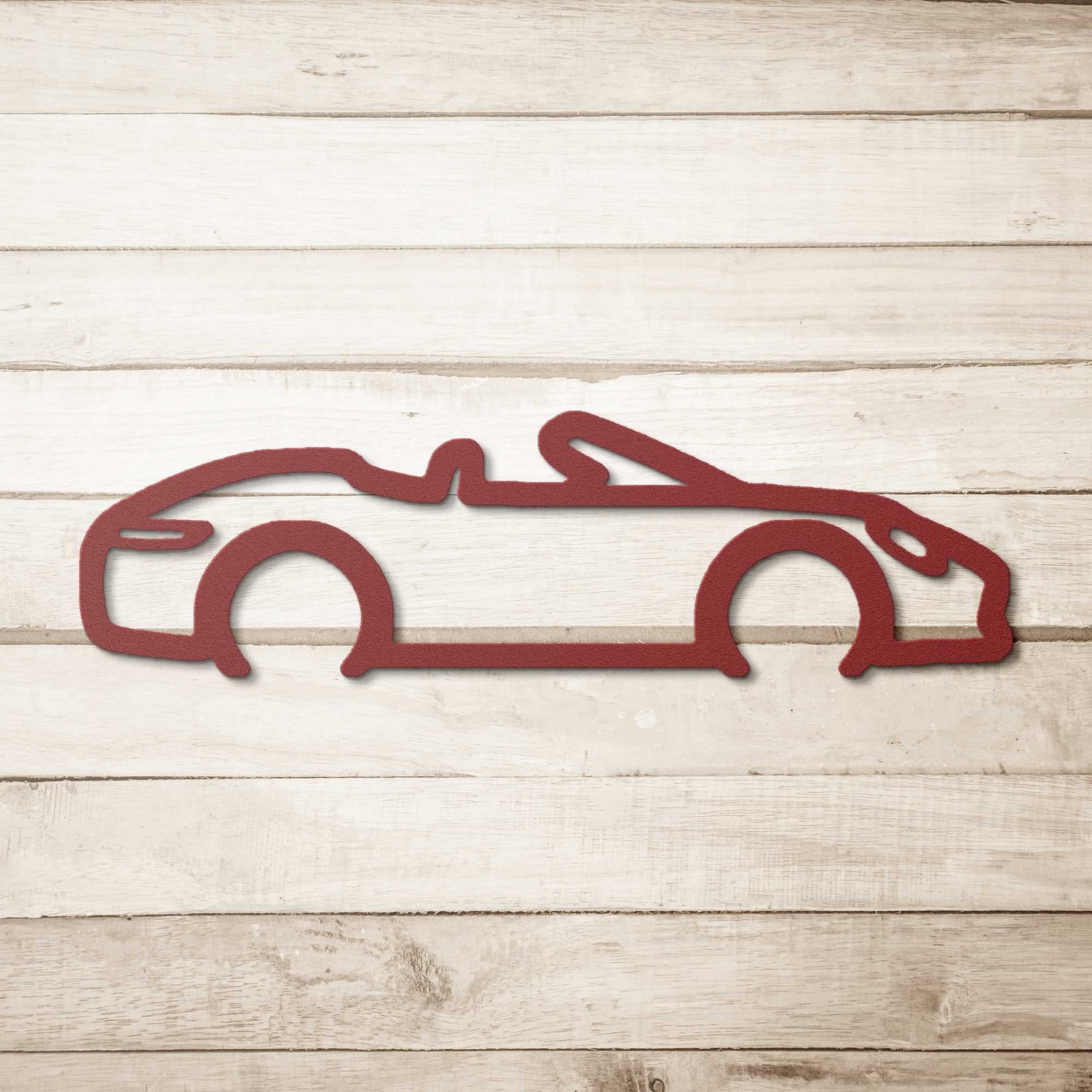 Red powder-coated steel automotive metal wall art featuring a convertible silhouette on a wooden background