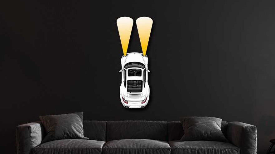 PCAR Headlights White metal wall art showing a white car with yellow headlights on a dark wall above a gray sofa in a modern living room