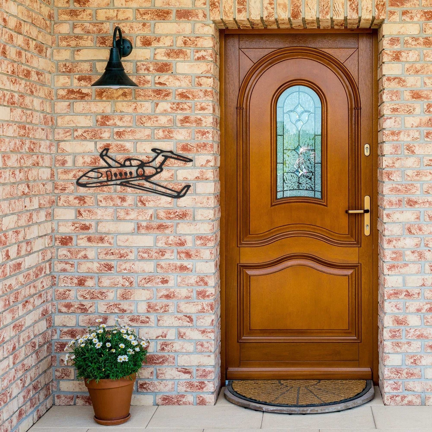 Elegant metal sign of a private jet mounted on a brick wall next to a wooden door with a potted plant below.