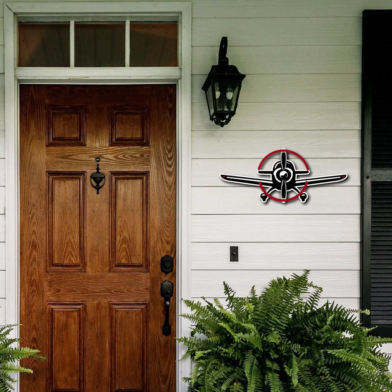 Multicolor metal sign in the shape of a propeller plane mounted on a white exterior wall next to a wooden front door