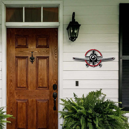 Multicolor metal sign in the shape of a propeller plane mounted on a white exterior wall next to a wooden front door