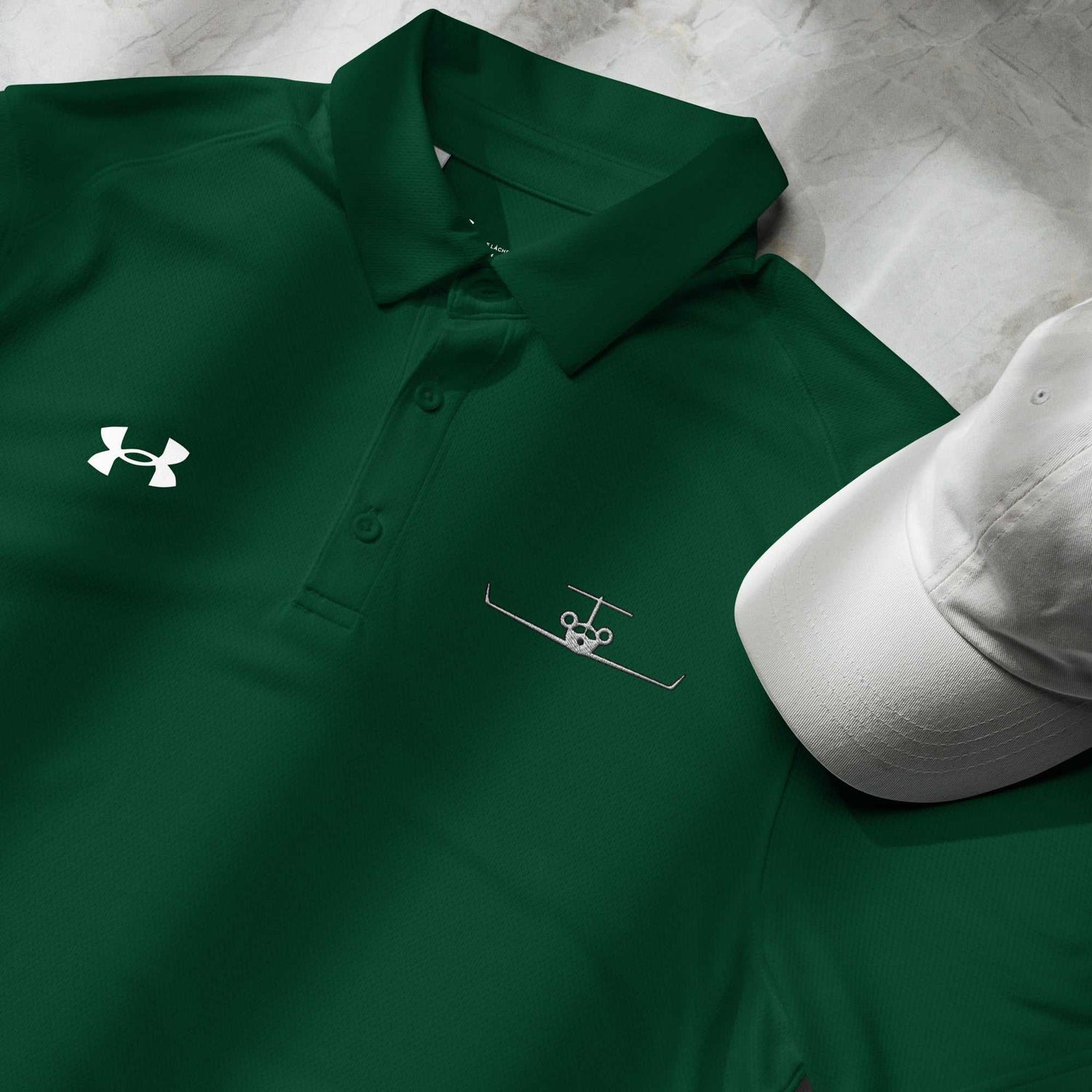 Green pilot polo shirt with embroidered private jet logo and Under Armour logo on chest next to a white cap
